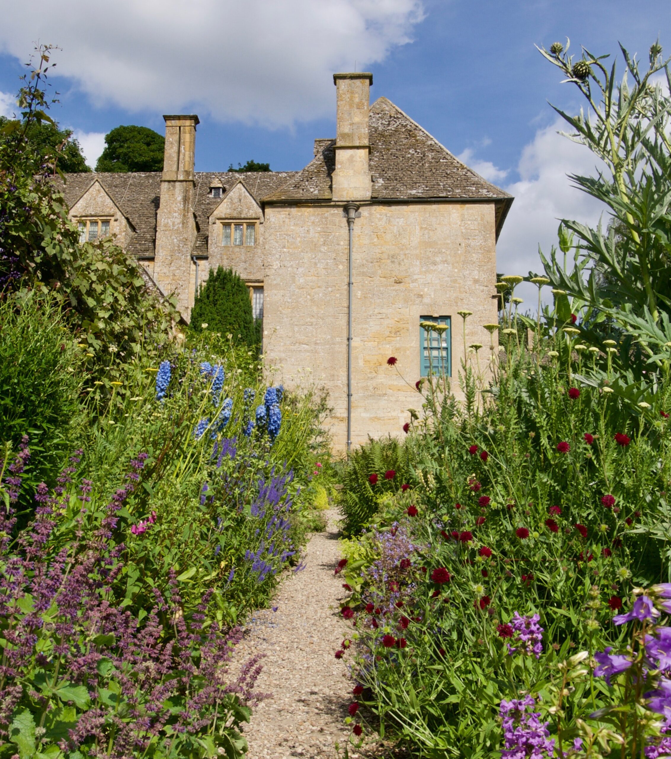 View of the side of the manor up a long path with colourful flowers lining the sides