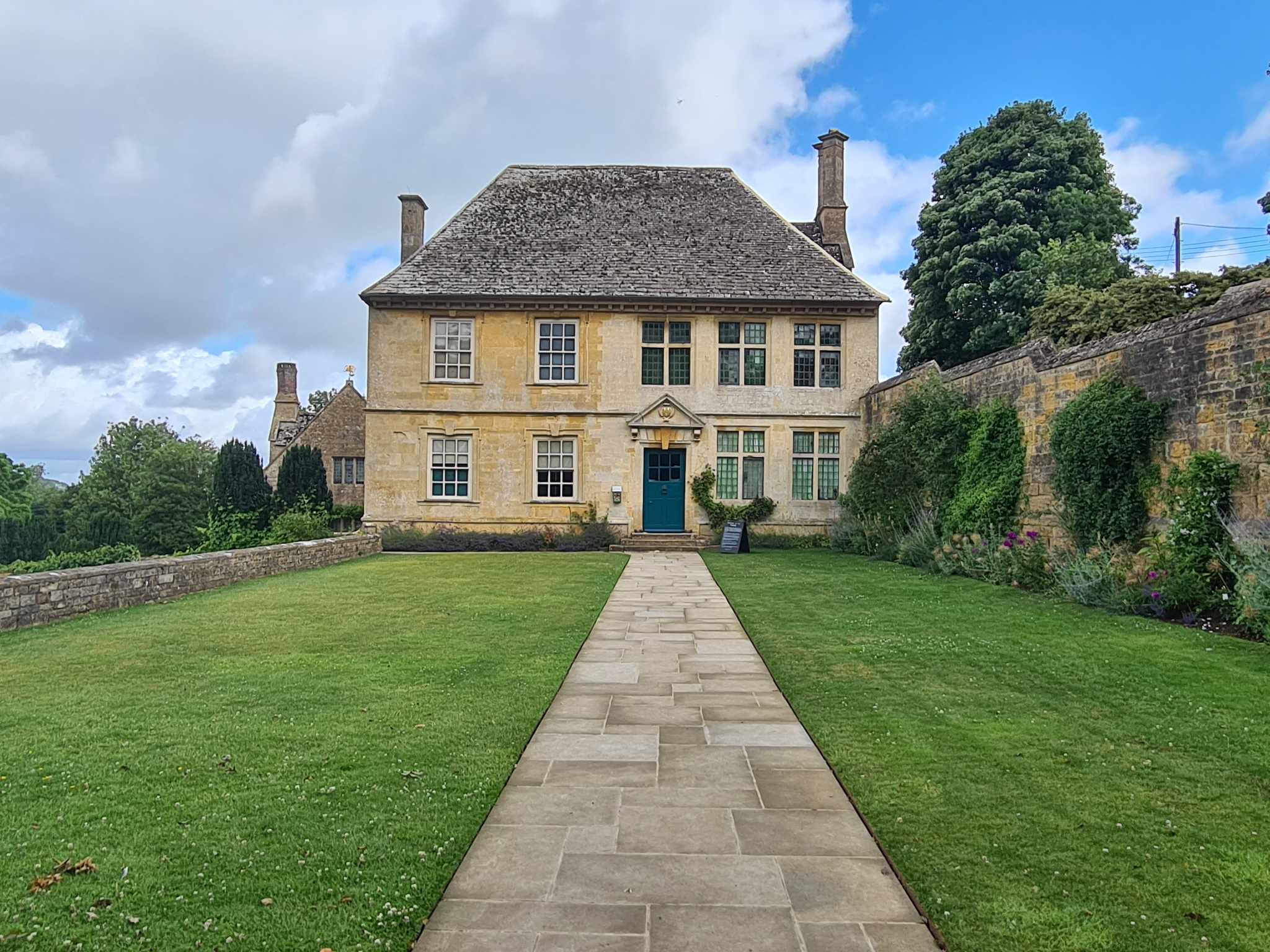View of Snowshill Manor from a long path, both made of Cotswold stone.