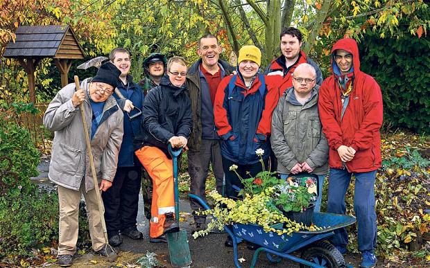 photo of a group of 9 wearing outdoor clothes in an autumnal outdoor setting, 2 people have garden tools