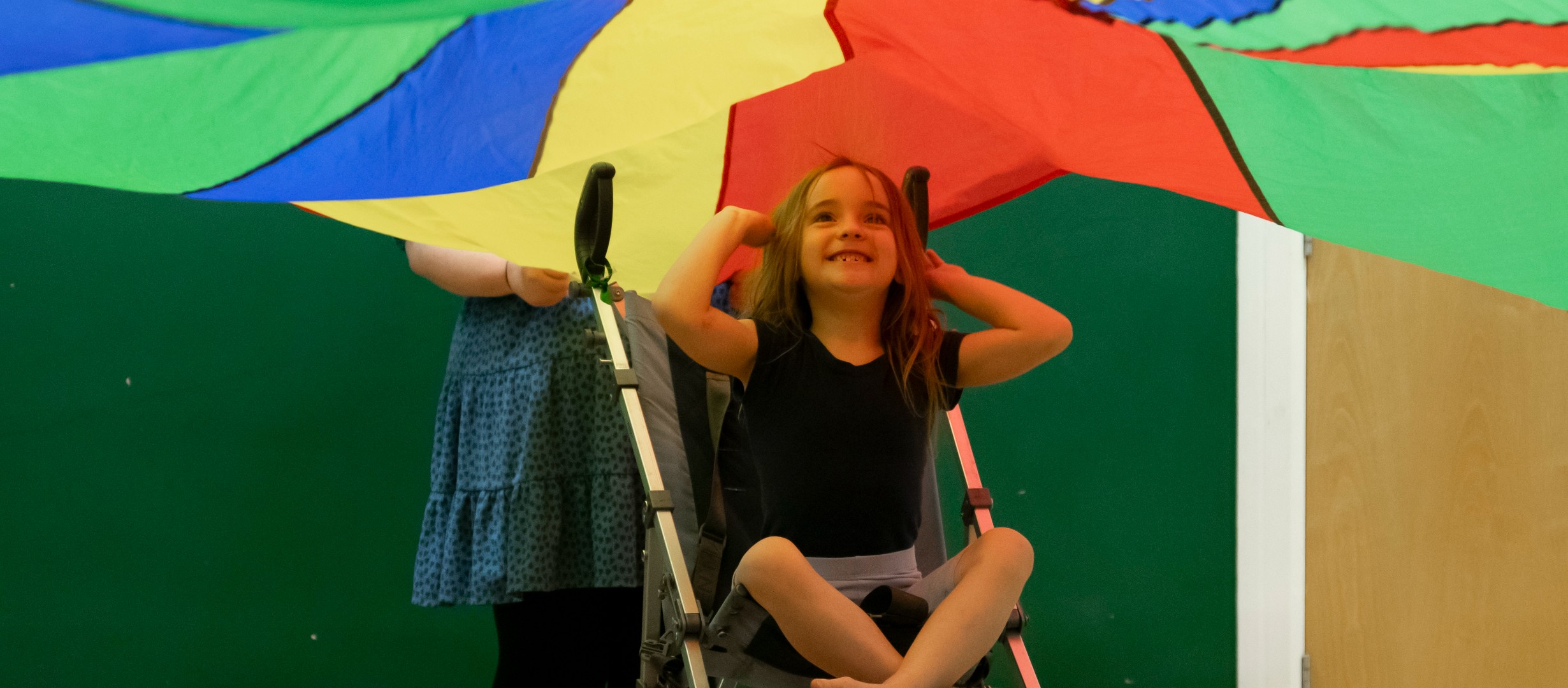 Female dancer sitting in her buggy underneath the parachute, reaching behind her head and smiling