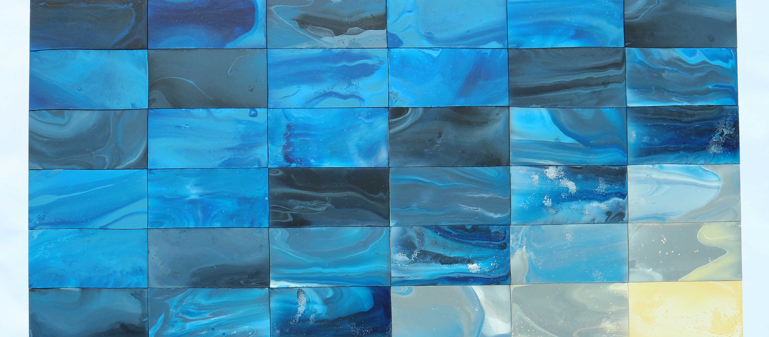 An abstract painting made up of thirty-six smaller rectangles. The rectangles are arranged in diagonal lines of colour moving from top left to bottom right in shades of blue, grey and then yellow, to represent waves moving towards the shore