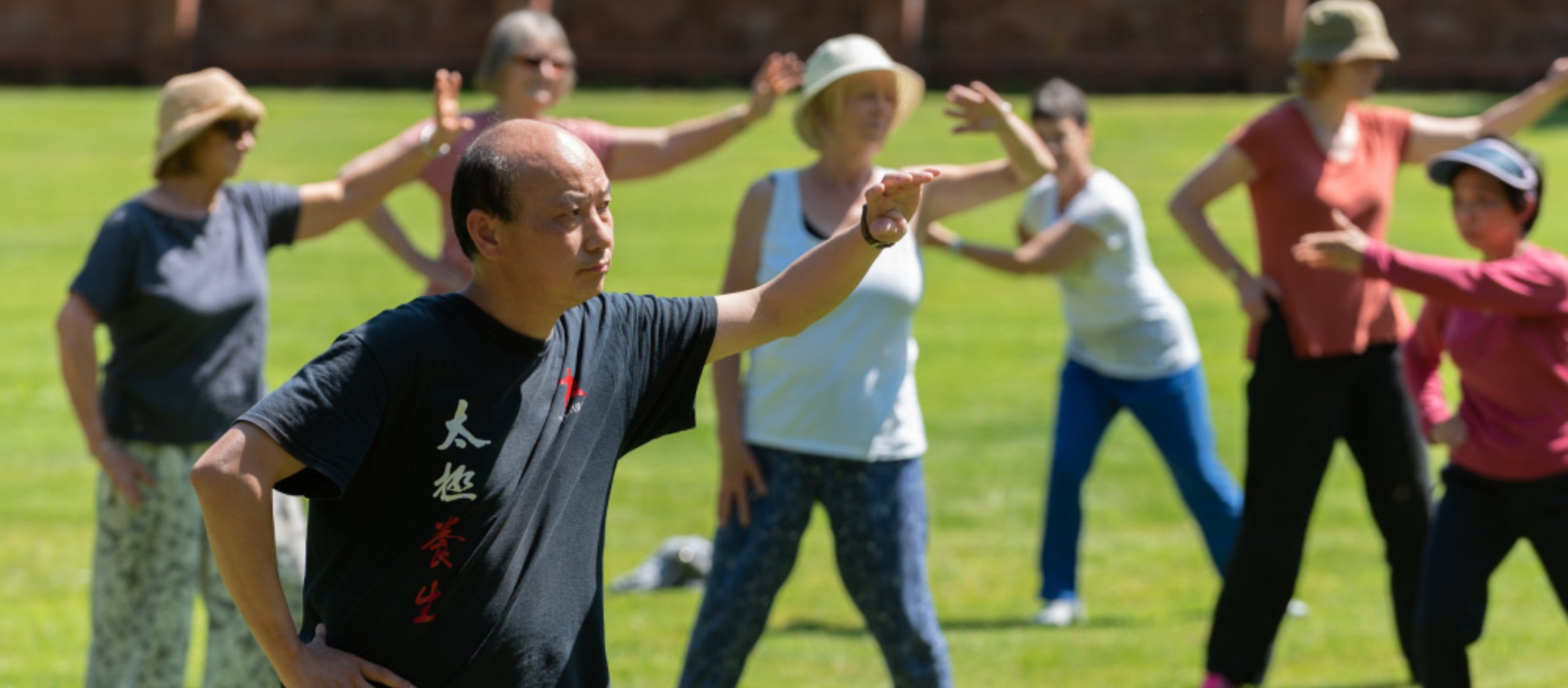 A group of people practice Tai Chi on a lawn at a National Trust property