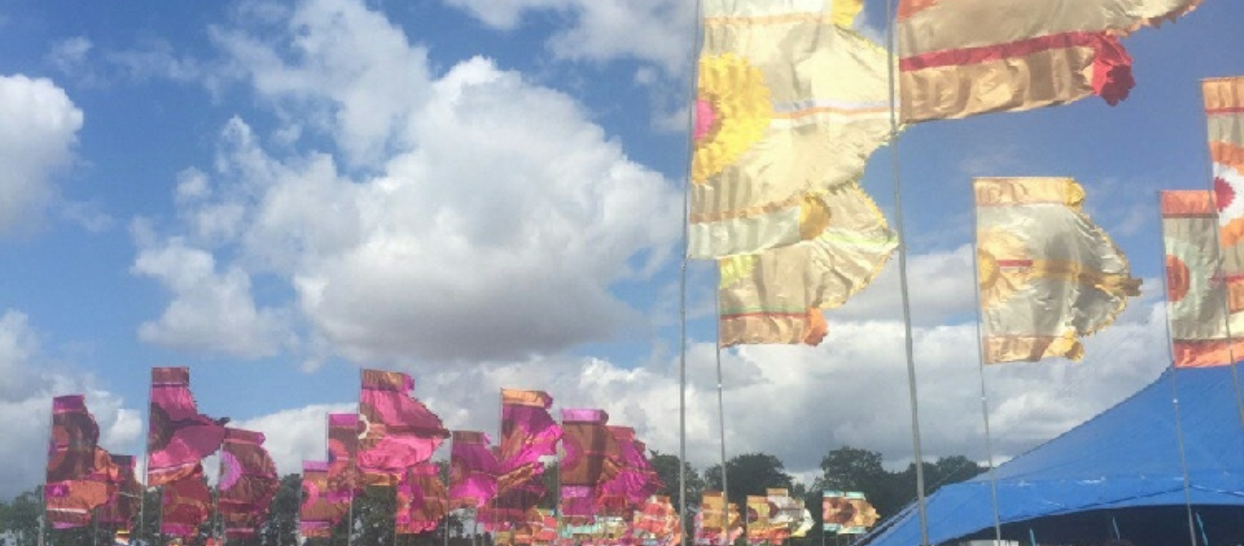 Image shows a number of large festival flags in yellow and pink against the blue, cloudy sky
