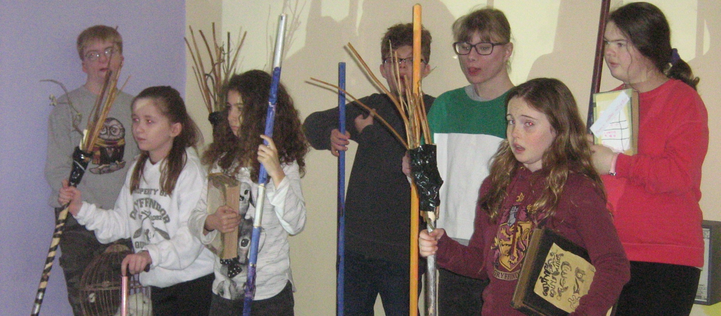 A group of young people stood in a group all holding broom sticks in their hands