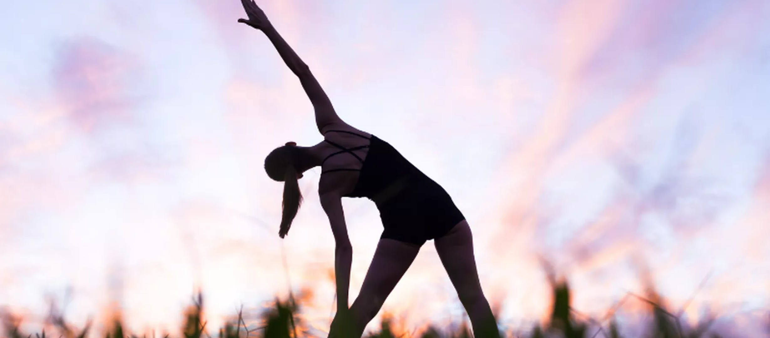 silhouette of a lady stretching, against a blurred sun set background