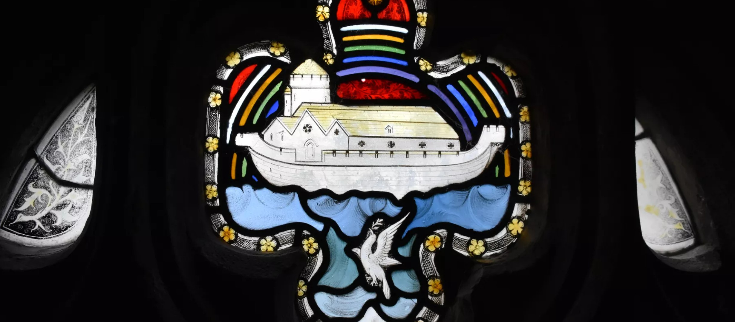 Stained glass window at Gloucester Cathedral depicting Noahs Ark with a dove underneath it, and a rainbow behind it