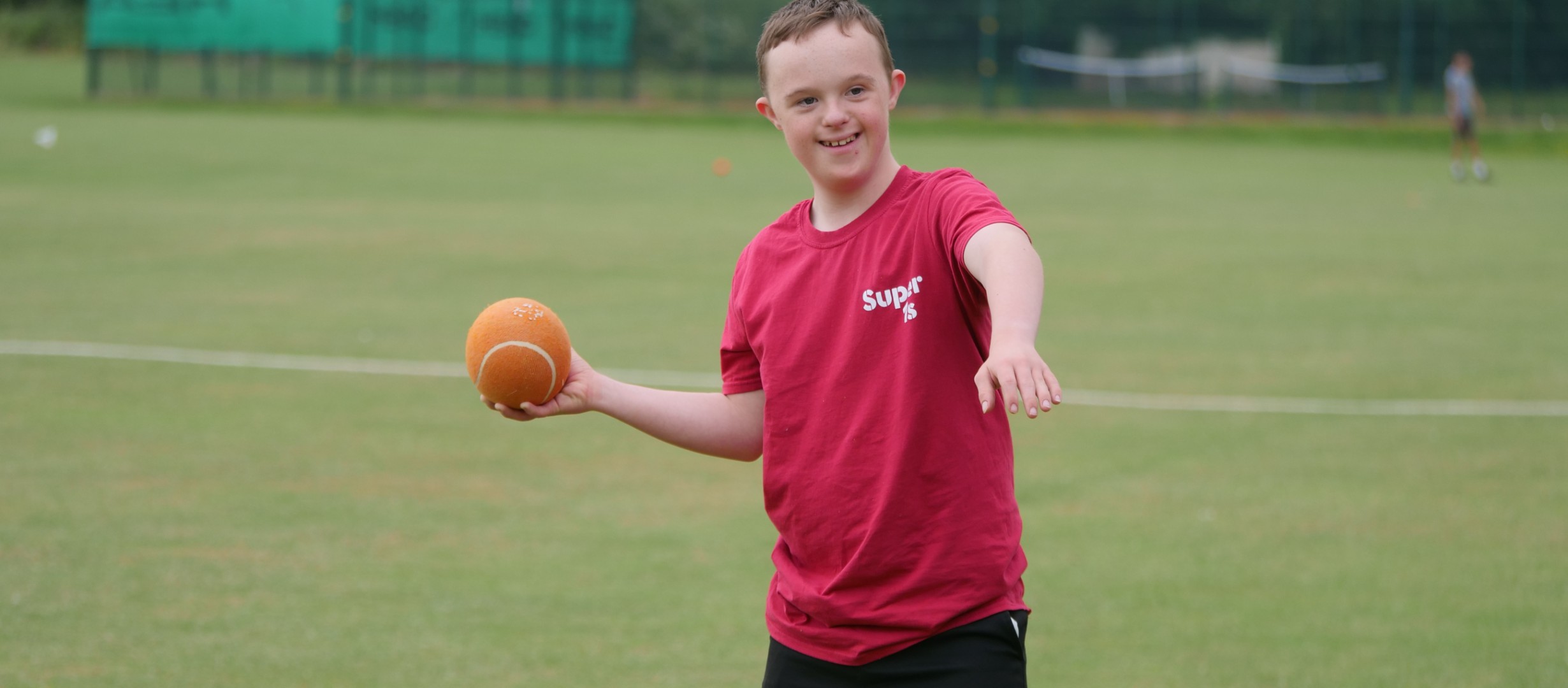 Young person holding orange cricket ball ready to bowl. 