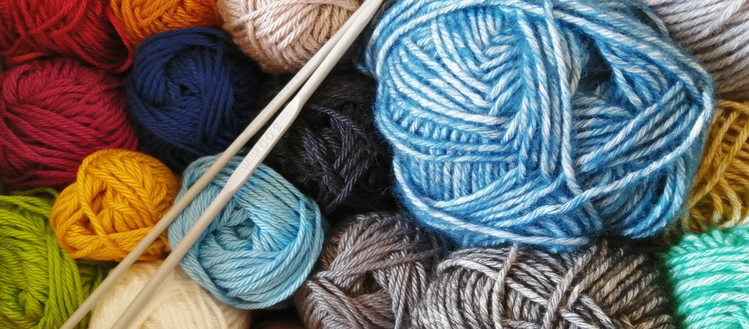 A pile of colourful wool with knotting needles