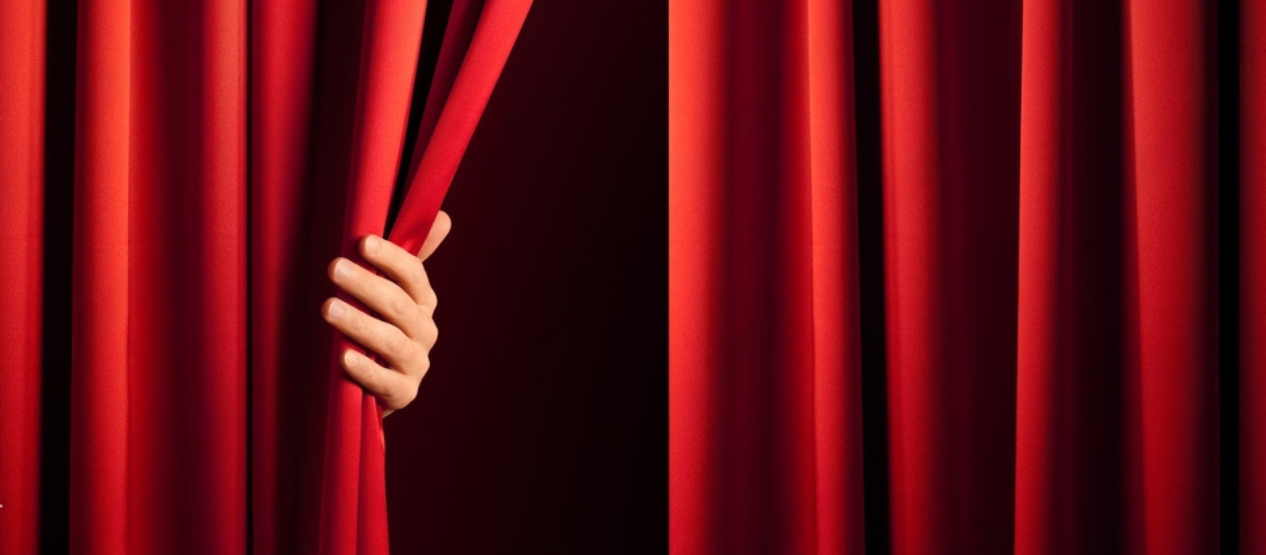 Hand holding back red theatre curtain