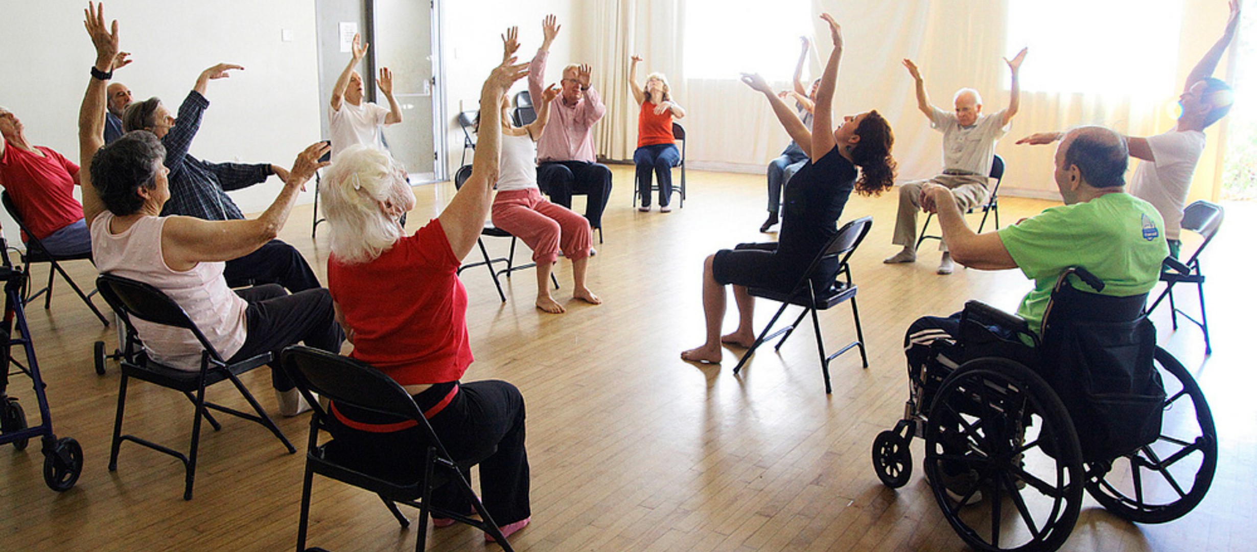 dance instructor doing arm movements with a class of seated participants 