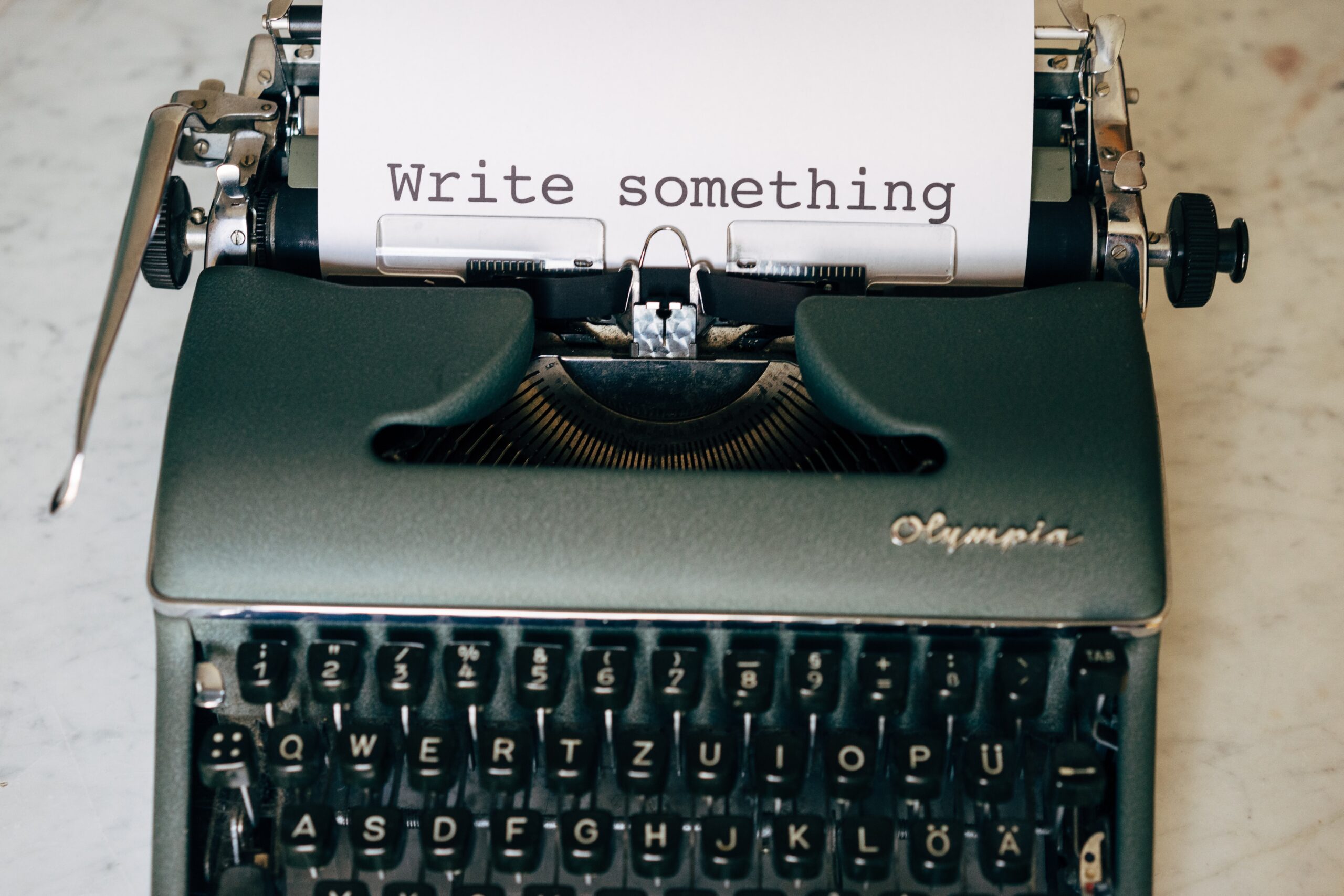 A photograpjh of a dark grey type writer on a marble surface. The words write something are displayed on the paper in the typewriter