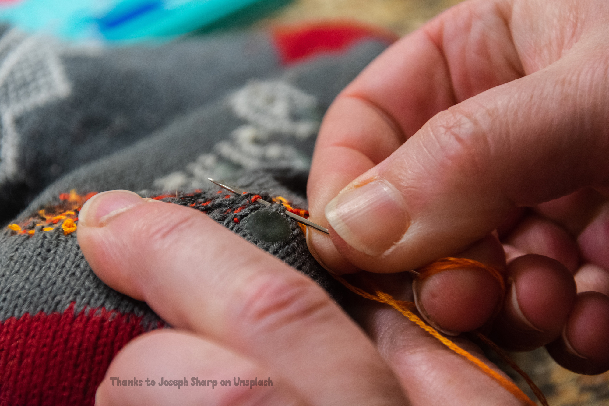 The photoif of a pair of hands mending a jumper with bright orange thread