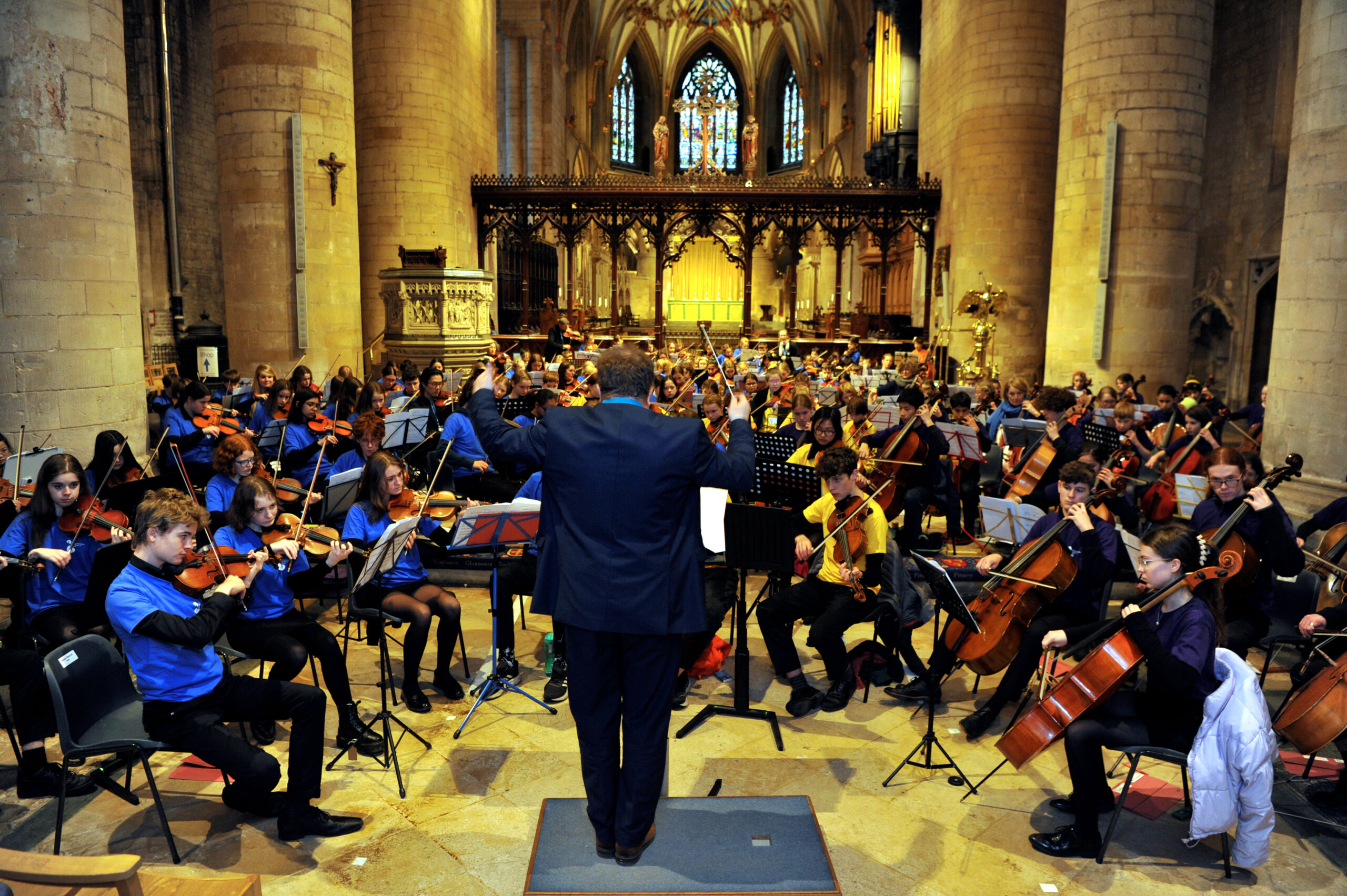photo of a conductor standing in front of a strings orchestra of young people in Tewkesbury Abbey