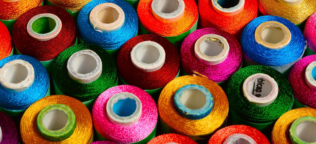 A colorful photograph of thread spools in vibrant colours which include yellow, pink, blue, green and red