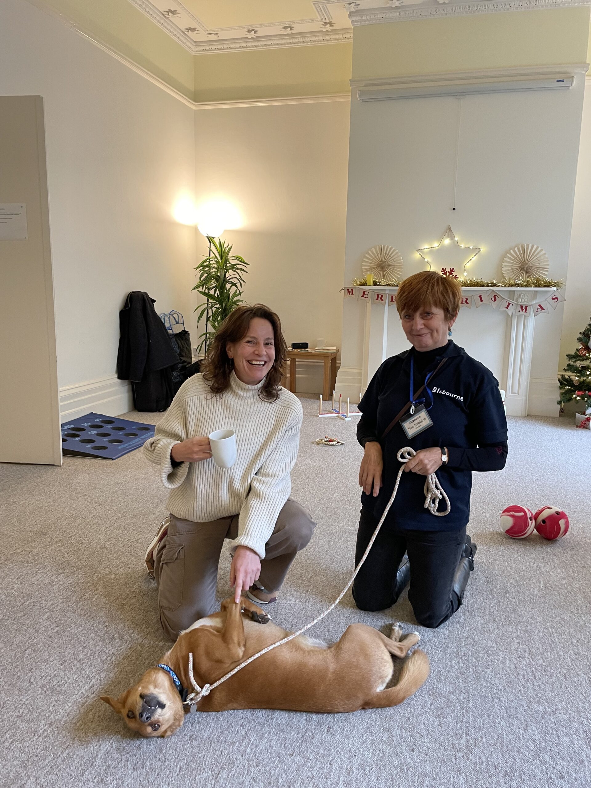 Two community wellbeing tutors knelt on the floor with the pets as therapy dog.
