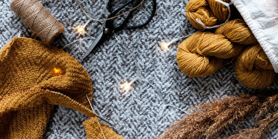 This is a photograph of brown colour threads, and a scarf and scissors on a grey. There are fairy lights winding inbetween