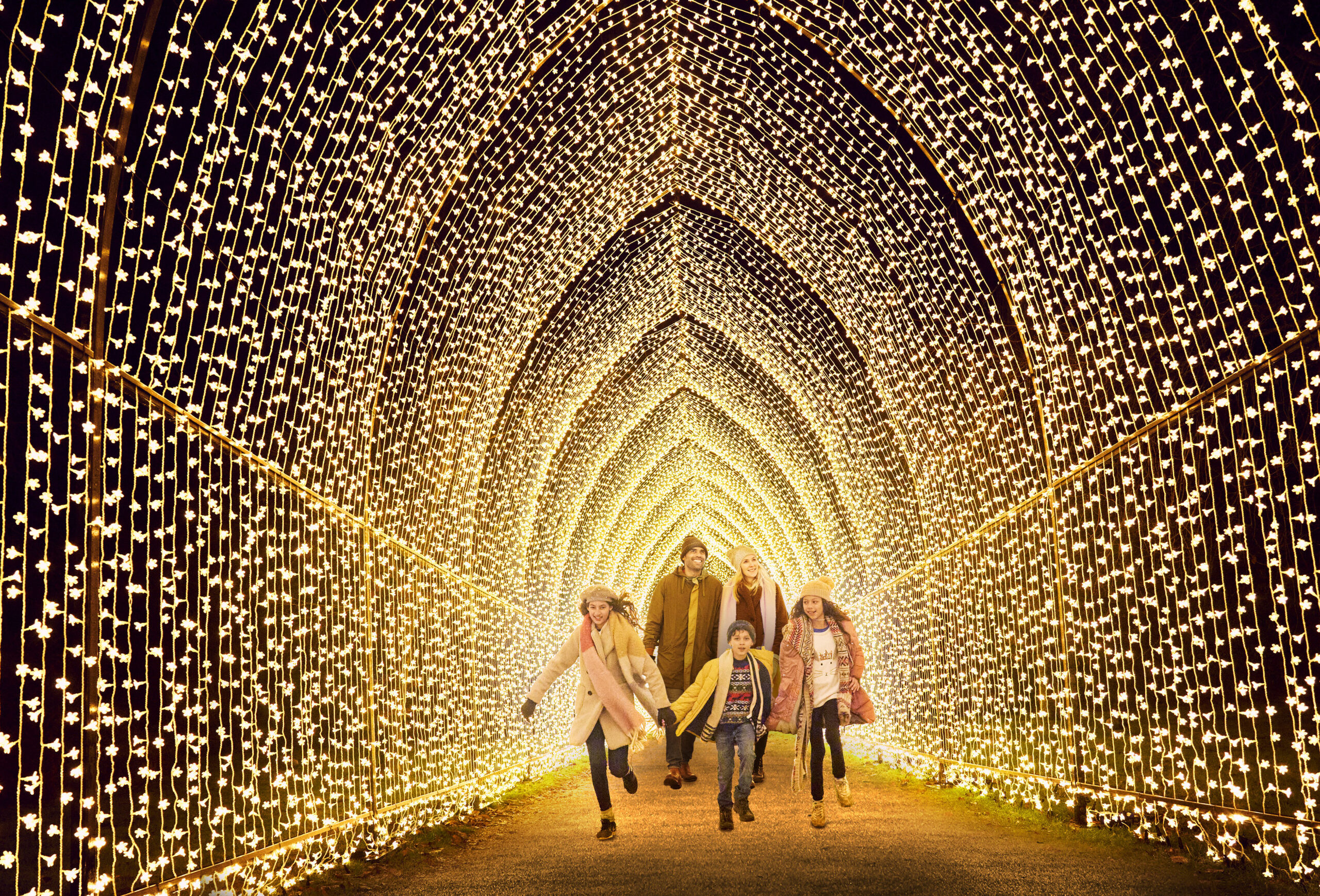 family walking beneath large Christmas light trail display