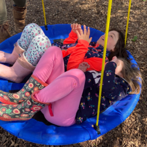 two children lying down on a large circular swing