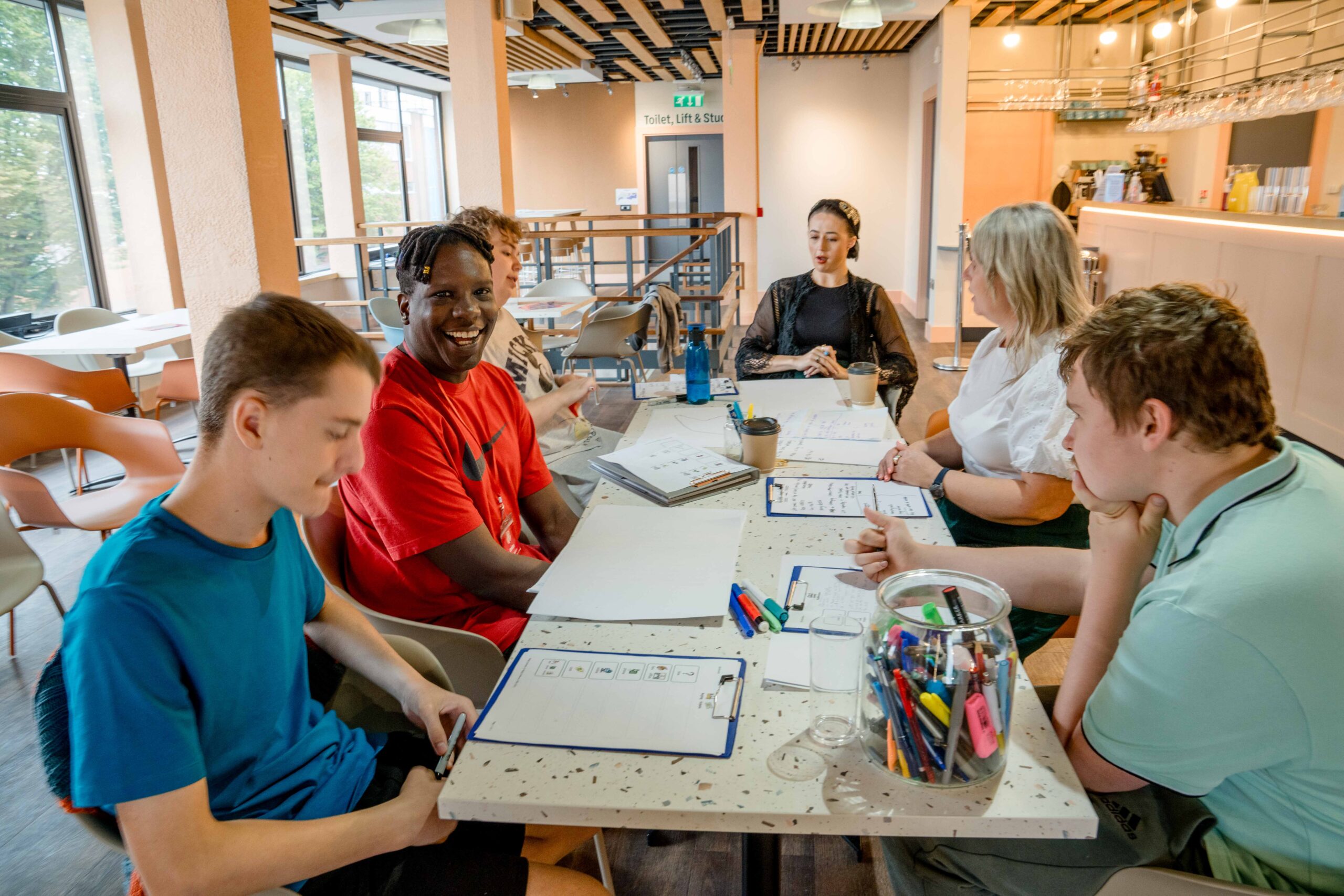 Group of people sat around a table with coloured pens and notebooks