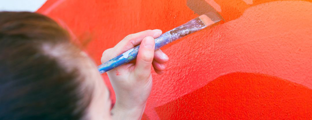 This is a photograph of a woman painting on a wall in red and orange paints