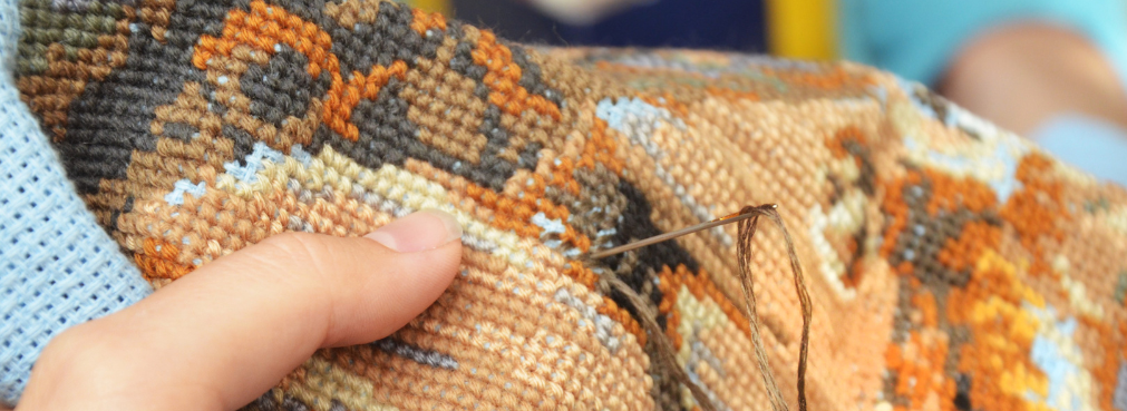 This is a photograph of a person making a cross stitch design in orange and brown tones