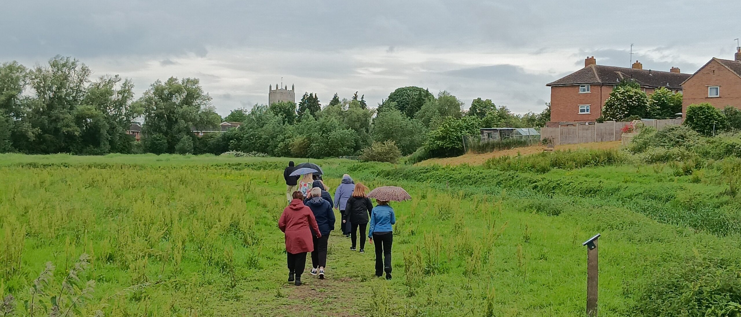 People walking in the north of Tewkesbury Nature Reserve. Tewkesbury Abbey is visible in the distance.