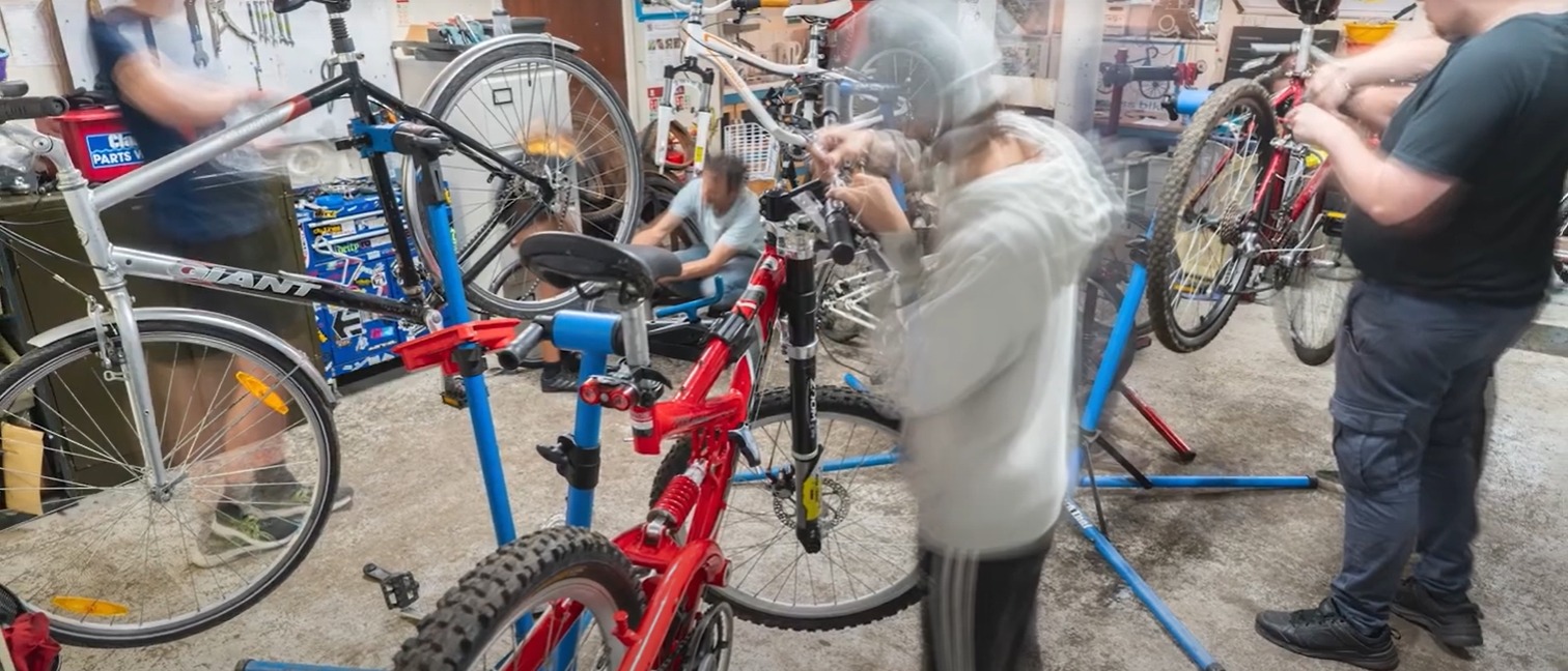 blurred image of some people in a bike workshop with bicycles on stands.