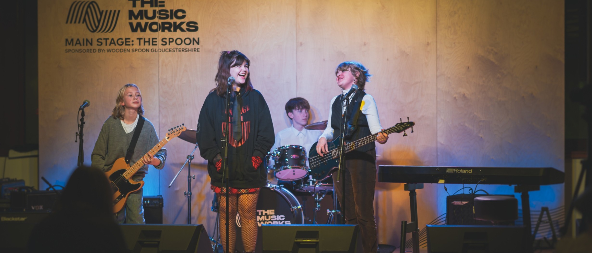 Young performers (2 guitarists, 1 signer and 1 drummer) on stage performing at one of our showcase events.