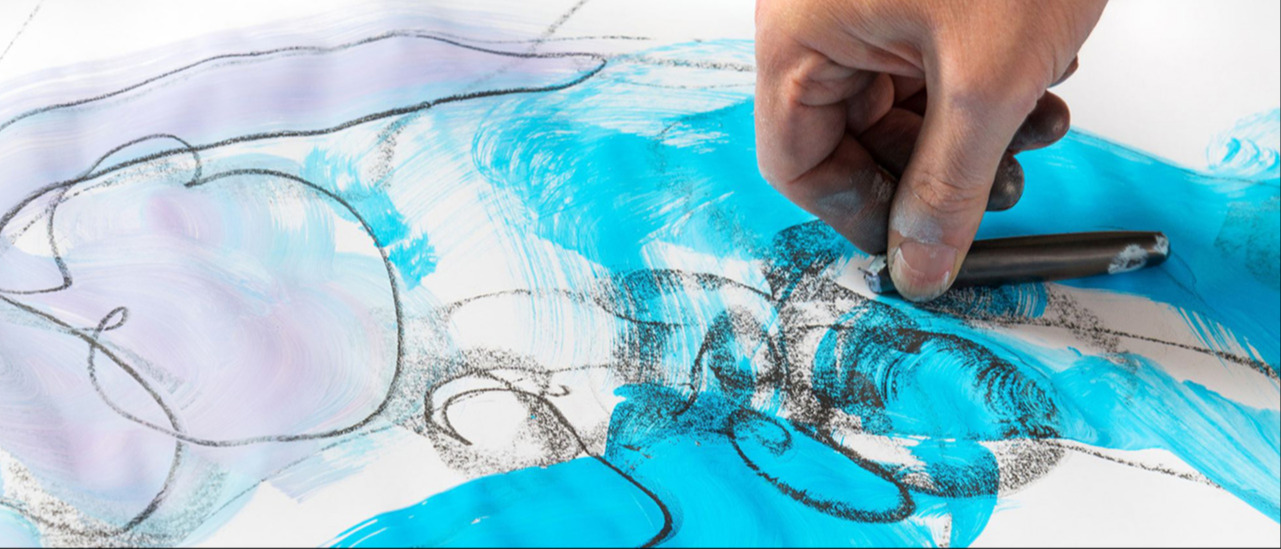 This is a photograph of a person drawing something experimental with charcoal and blue inks