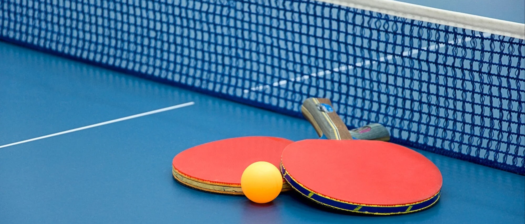 Photo of two table tennis bats and a table tennis ball, on a table.